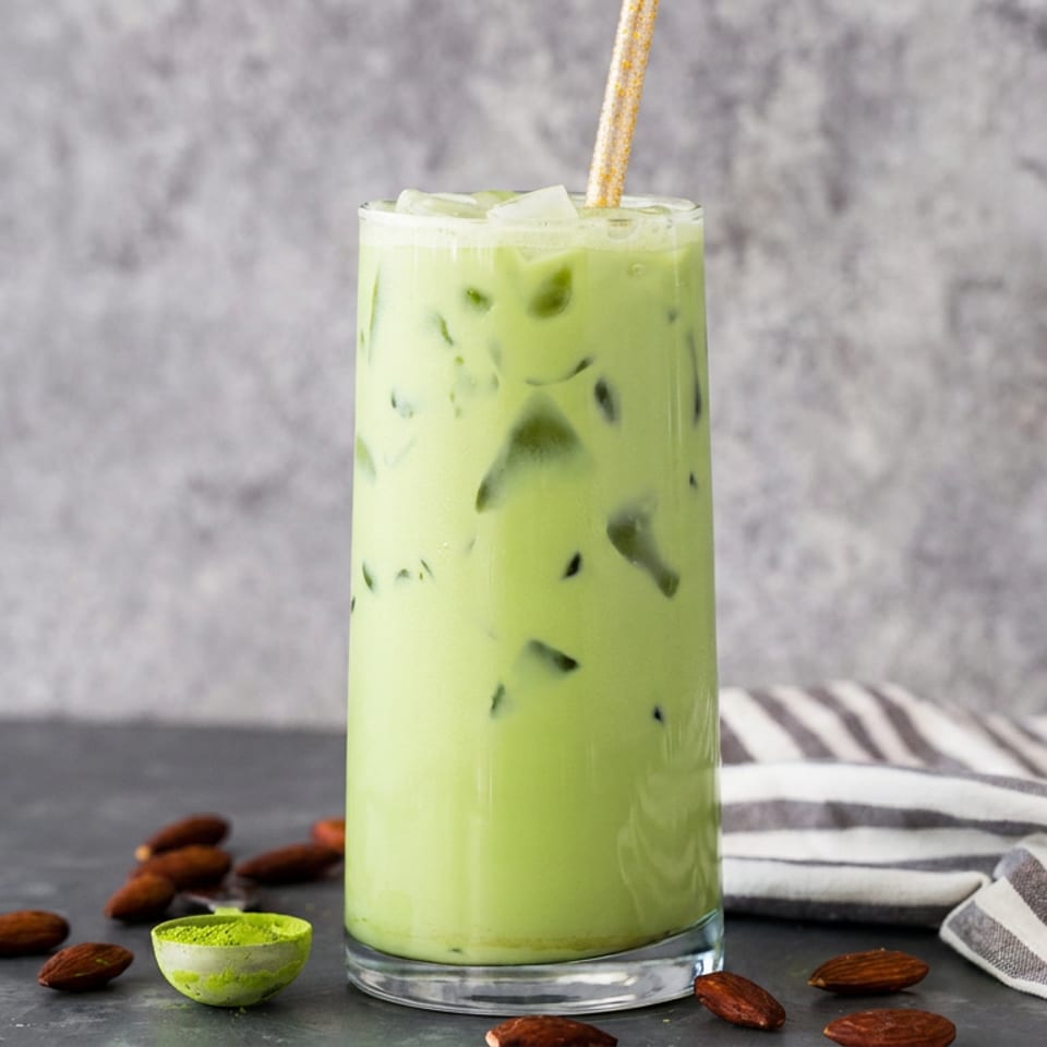 Iced green matcha latte in a tall glass with a straw, surrounded by almonds and a striped napkin.