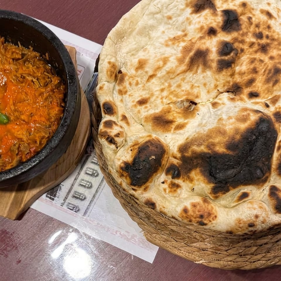 Basket of charred naan bread beside a black bowl of orange curry garnished with a green chili.