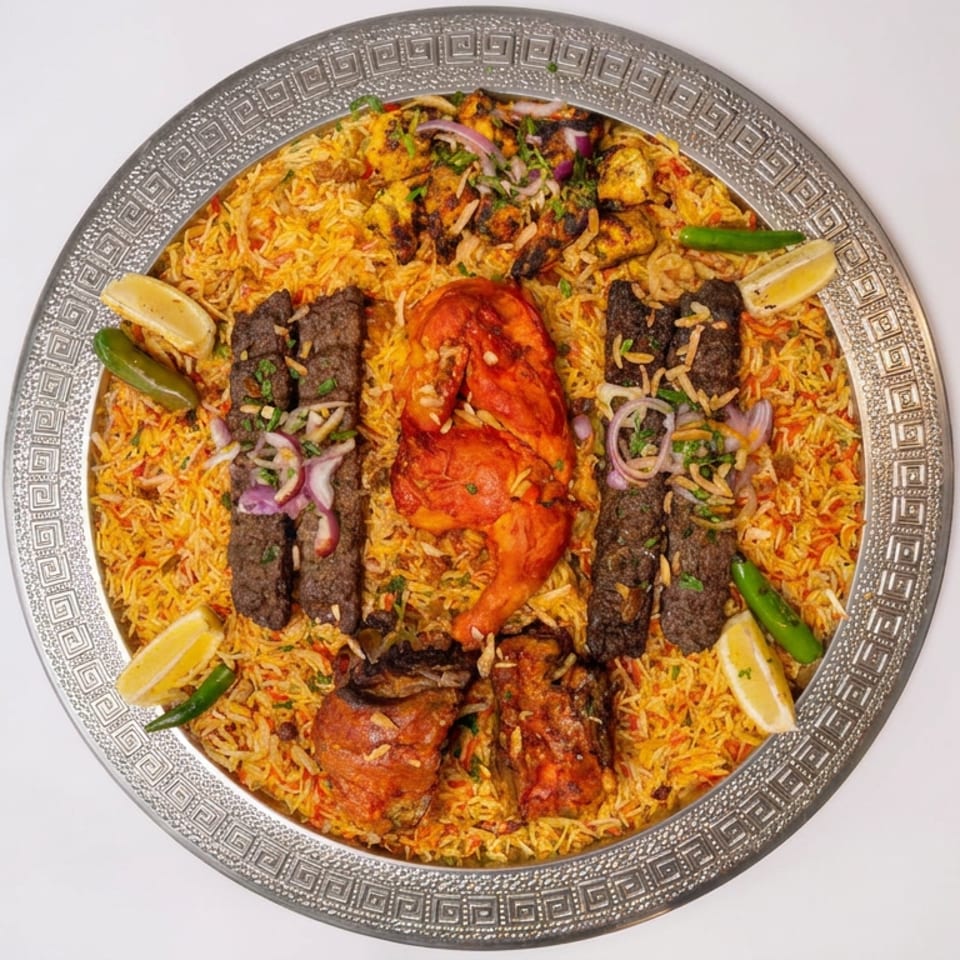 Overhead view of a platter of spiced rice topped with grilled meat, roasted chicken, herbs, chilies, and lemon wedges.
