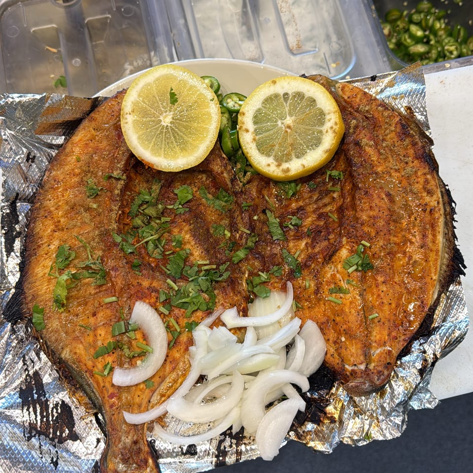 Grilled whole fish on foil garnished with lemon slices, cilantro, sliced onions, and green chilies.
