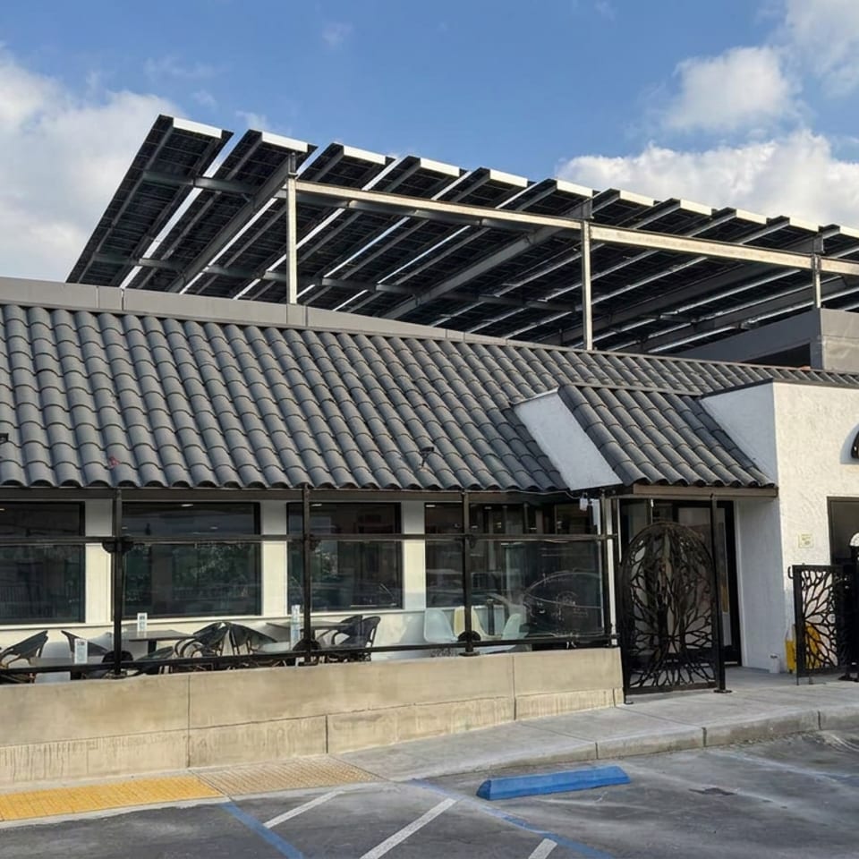 Mandi Xpress restaurant exterior with tiled roof, outdoor patio seating, decorative gates, and rooftop solar panels.