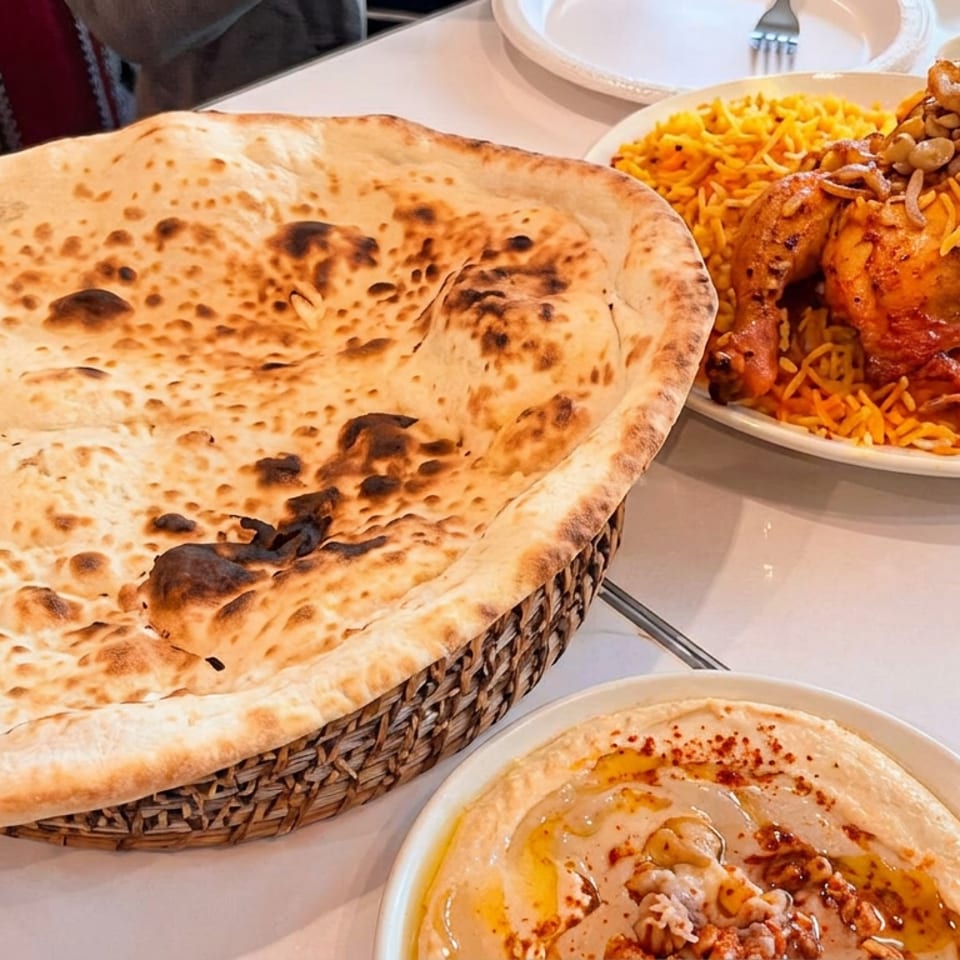 Freshly baked flatbread, roasted chicken over saffron rice, and hummus served on a restaurant table.