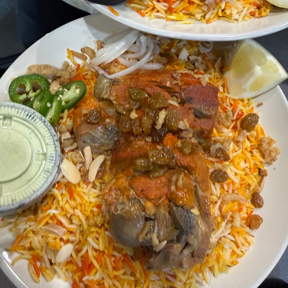 Large platter of colorful rice topped with grilled meats, onions, jalapeños, almonds, and lemon, accompanied by sauces.