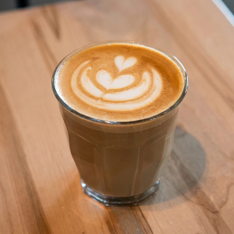 Glass of latte with heart-shaped foam art on a wooden café table.