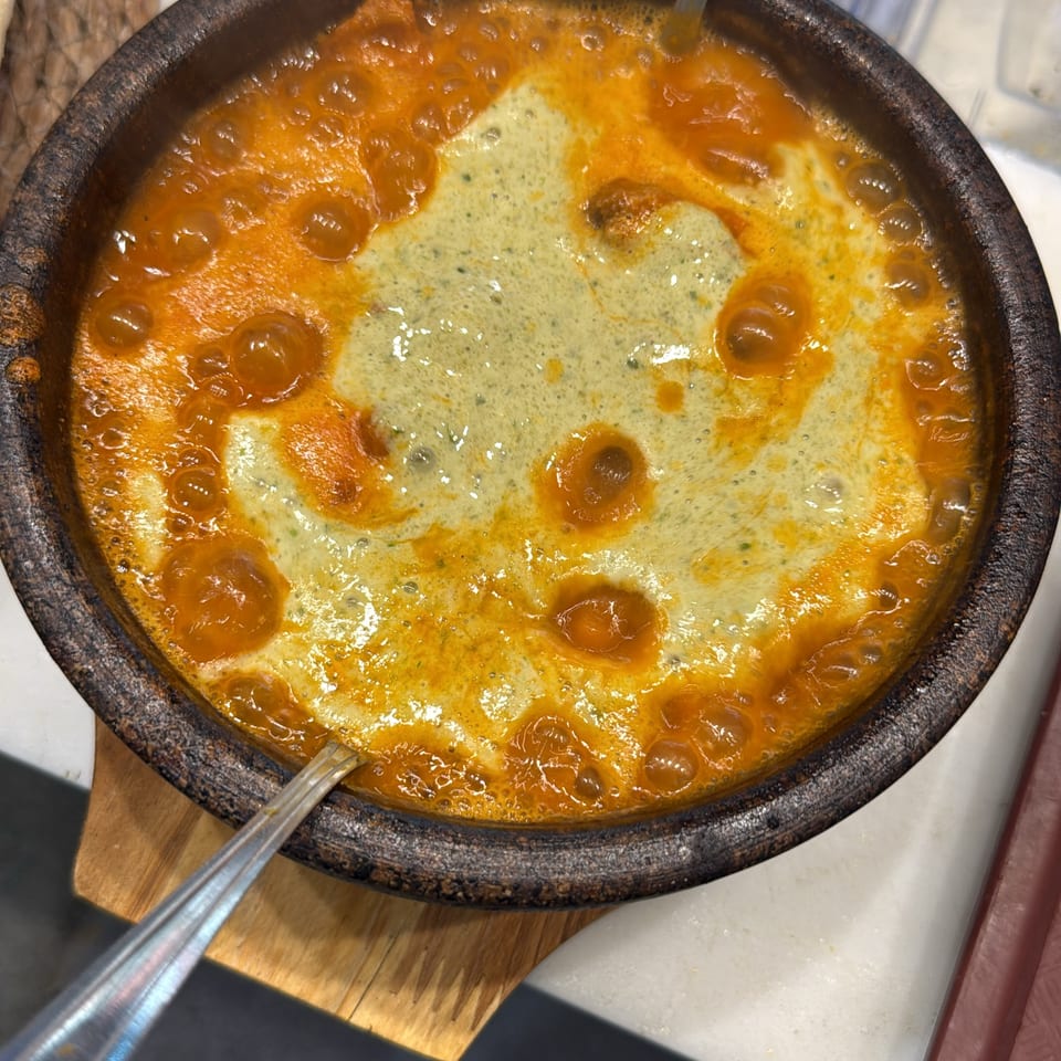 Close-up of bubbling orange curry with creamy herb sauce in a rustic serving dish, accompanied by a serving spoon.